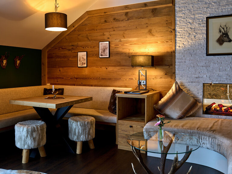Abendliche Stimmung im Wohnbereich der Top of Suite Jagasitz Plus mit Kachelofen-Optik, Holzverkleidung und stilvoller Beleuchtung im Hotel Oswald.