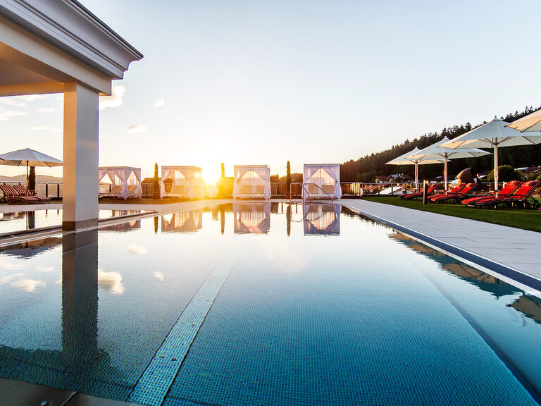 Der Infinity-Pool im Hotel Oswald mit kristallklarem Wasser, luxuriösen Bali-Betten und Sonnenliegen, perfekt für entspannte Momente bei Sonnenuntergang.
