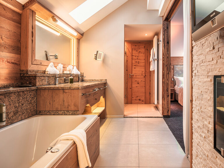 Das luxuriöse Badezimmer der Top of Suite Jagasitz Plus im Wellnesshotel Oswald mit Granitwaschtisch, Badewanne und Kaminblick.
