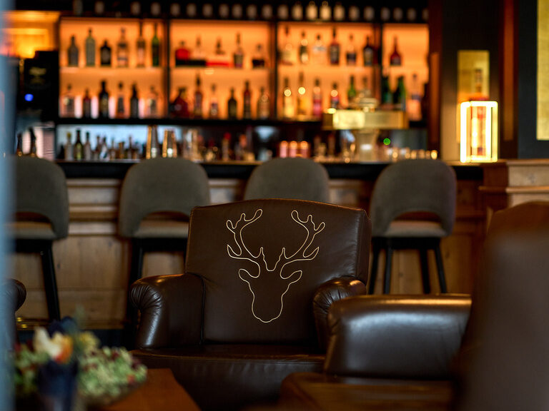 Ein brauner Ledersessel in der Hotellounge steht vor der eleganten Bar im Landromantik Hotel Oswald Bayerischer Wald.