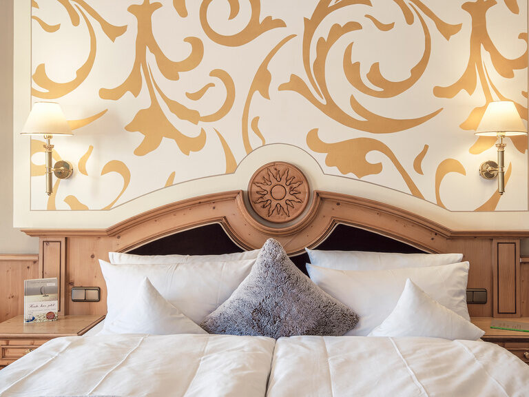 Das Bett mit eleganter Holzkopfleiste und kunstvoller Wandgestaltung im Doppelzimmer Landgold des Hotel Oswald Bayerischer Wald.