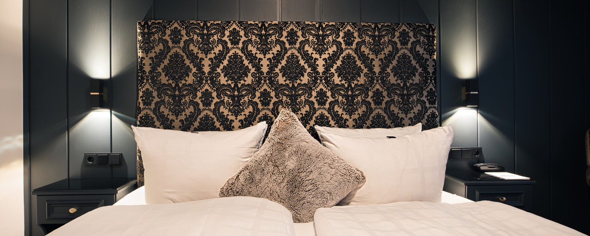 Das gemütliche Doppelbett im Schlafensbereich des Doppelzimmer Spatz im Hotel Oswald, mit gemütlichen Kissen und Nachttisch.