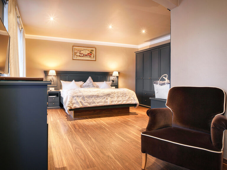 Das Doppelzimmer Roulette mit warmen Holztönen, stimmungsvoller Beleuchtung und großzügigem Bett im Hotel Oswald.