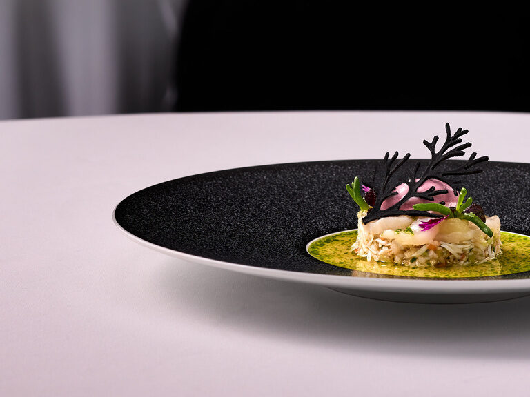 Ein kunstvoll angerichtetes Fine-Dining-Gericht auf einem schwarzen Teller im Hotel Oswald im Bayerischen Wald.