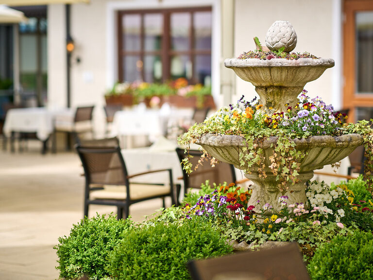 Die Gartenterrasse im Hotel Oswald mit blühendem Springbrunnen, üppigem Grün und stilvollen Sitzmöglichkeiten für entspannte Stunden im Freien.