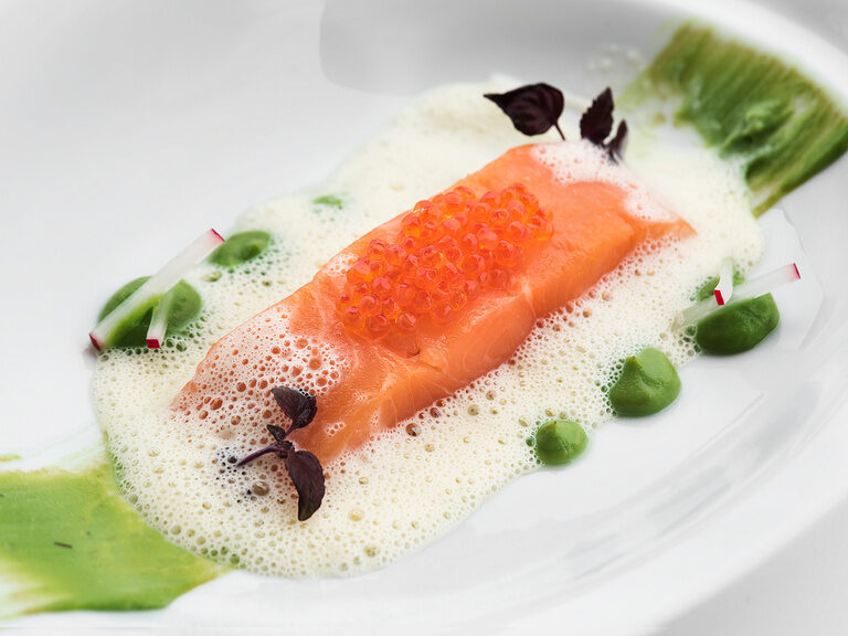 Ein kunstvoll angerichteter Lachs mit Kaviar und feinem Schaum, begleitet von erfrischenden grünen Akzenten im Restaurant Hotel Oswald.