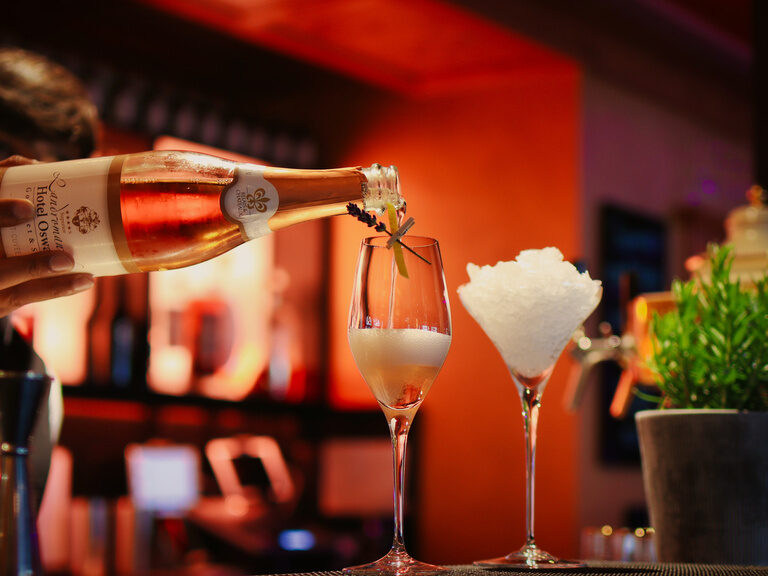 Das Einschenken eines edlen Rosé-Sekts in ein elegantes Champagnerglas, stilvoll garniert mit einem frischen Zweig in der Bar im Hotel Oswald.