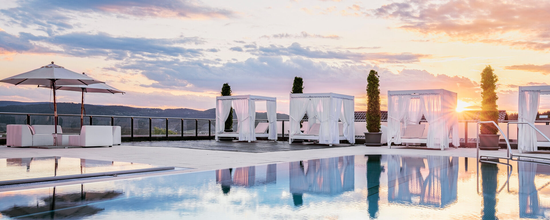 Die traumhafte Poollandschaft mit Himmelsspiegelung im Hotel Oswald, luxuriösen Bali-Betten und atemberaubendem Sonnenuntergang.