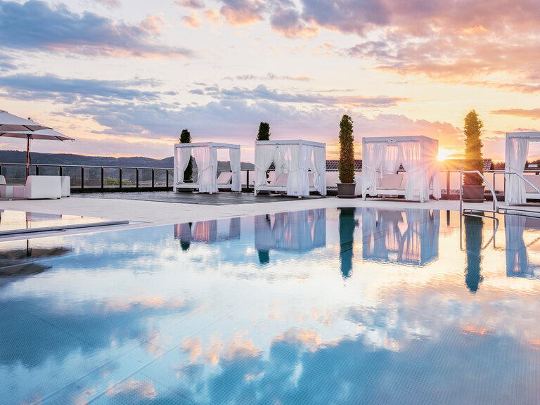 Die traumhafte Poollandschaft mit Himmelsspiegelung im Hotel Oswald, luxuriösen Bali-Betten und atemberaubendem Sonnenuntergang.