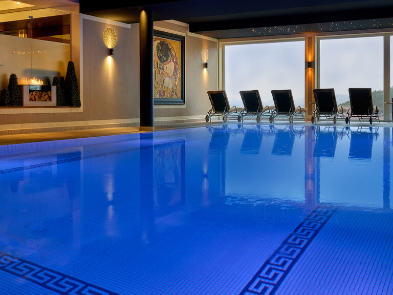 Der Innenpool im Hotel Oswald leuchtet im intensiven Blau zusätzlich bietet es Liegestühle mit Blick aus dem Panoramafenster.
