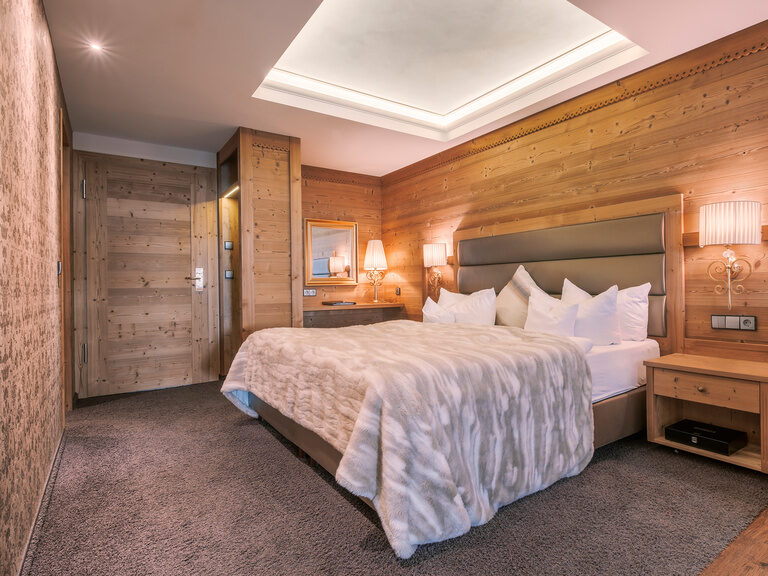 Die gemütliche Kuschelsuite im Hotel Oswald mit edler Holzverkleidung, luxuriösem Doppelbett und flauschiger Tagesdecke für eine warme Atmosphäre.