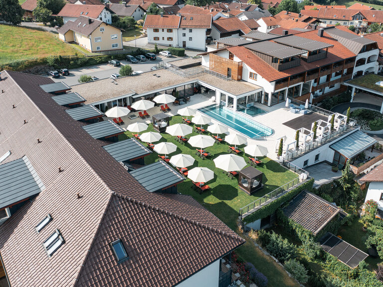 Das Hotel Oswald aus der Luft mit weitläufigem weitläufigem Poolbereich, Sonnenterrasse und grüner Gartenlandschaft.