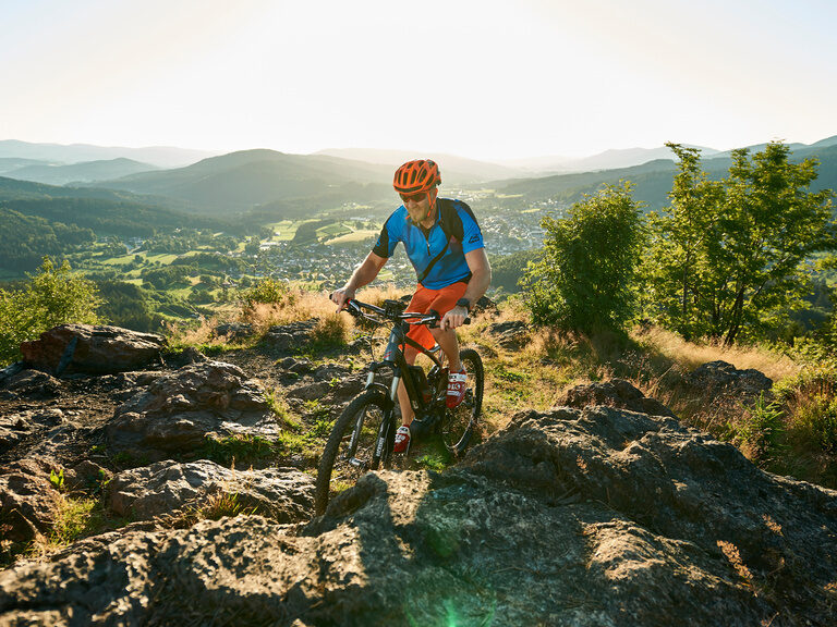 Ein Mann auf einem Mountainbike fährt einen felsigen Pfad im Bayrischen Wald hinunter.