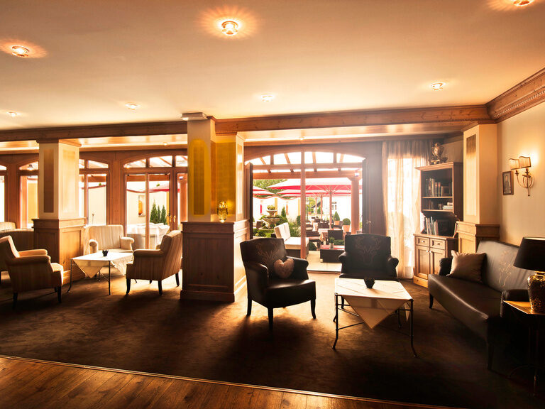 Die Hotel-Lounge im Hotel Oswald bietet viele bequeme Sitzmöglichkeiten, warme Holzelemente und einen direkten Zugang zur Terrasse.
