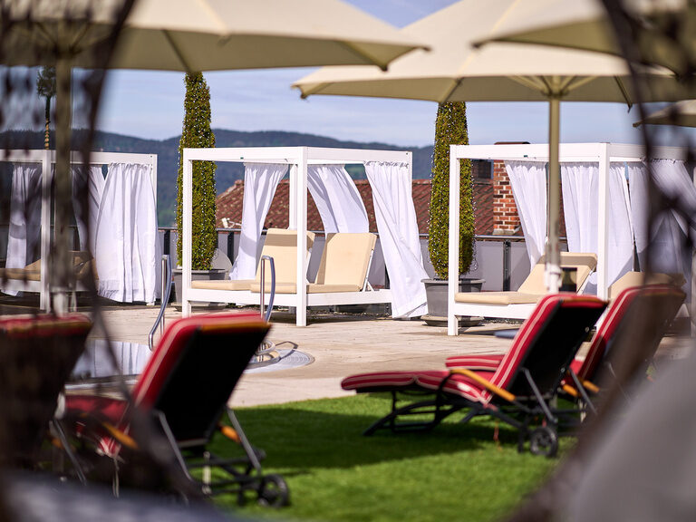 Ein Paar Liegestühle unter Sonnenschirmen - Erholung im Wellness-Garten des Landromantik Hotel Oswald.