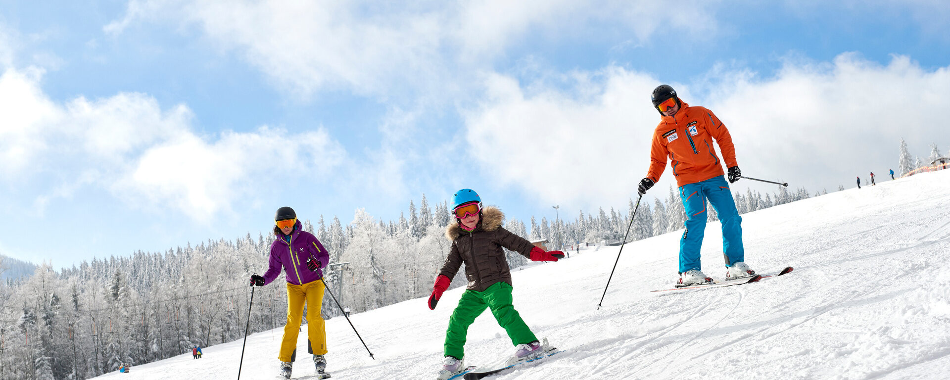 Eine Familie fährt mit Ski den verschneiten Hang hinunter - perfekte Winterlandschaft im Bayerischen Wald.