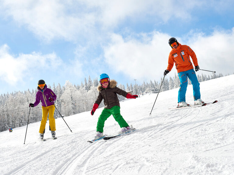 Eine Familie fährt mit Ski den verschneiten Hang hinunter - perfekte Winterlandschaft im Bayerischen Wald.