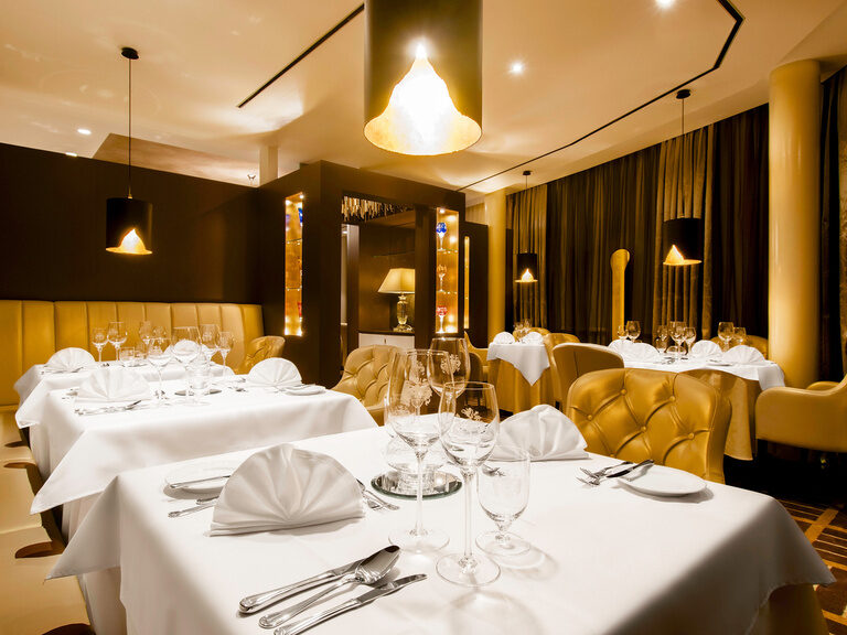 Die Mariastube im Hotel Oswald besticht durch schlicht, aber edel gedeckte Tische, goldene Möbel und eine stimmungsvolle Beleuchtung für ein gehobenes Genusserlebnis.