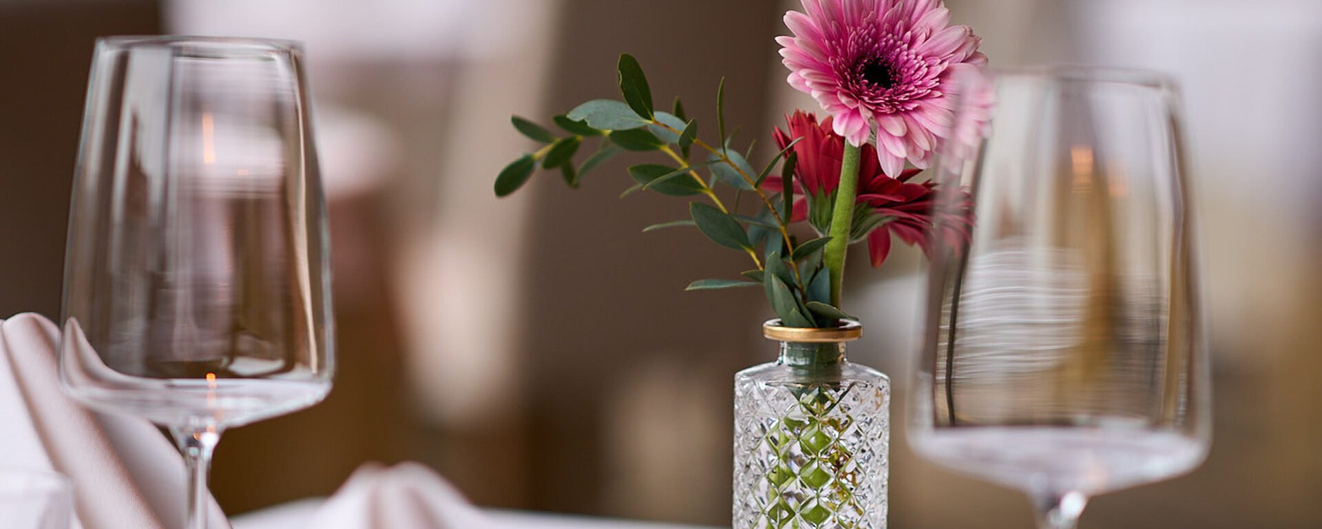 Stilvoll gedeckter Tisch mit eleganter Glasvase mit frischen Blumen für eine gemütliche Atmosphäre im Restaurant im Hotel Oswald Bayerischer Wald.