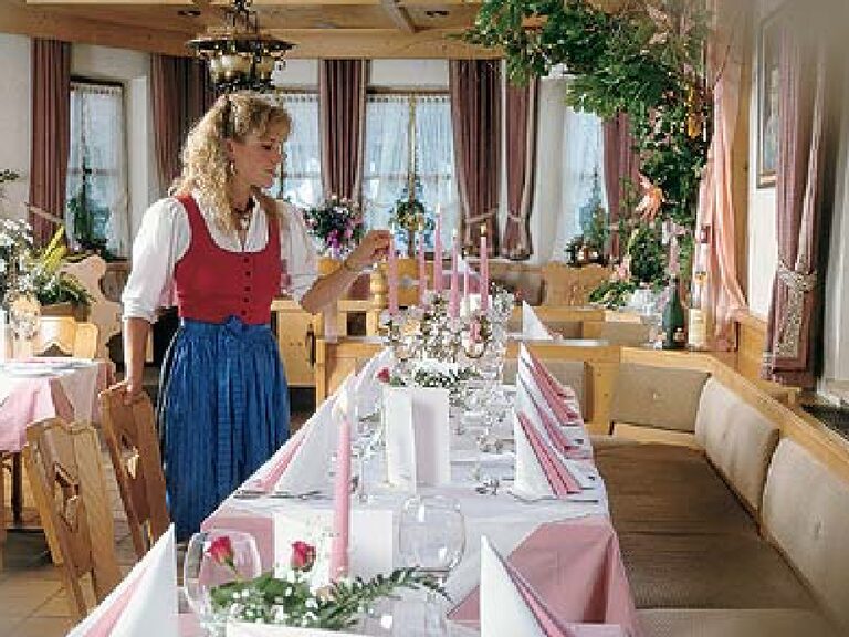 Frau in Tracht dekoriert festlich gedeckten Tisch im Hotel Oswald.