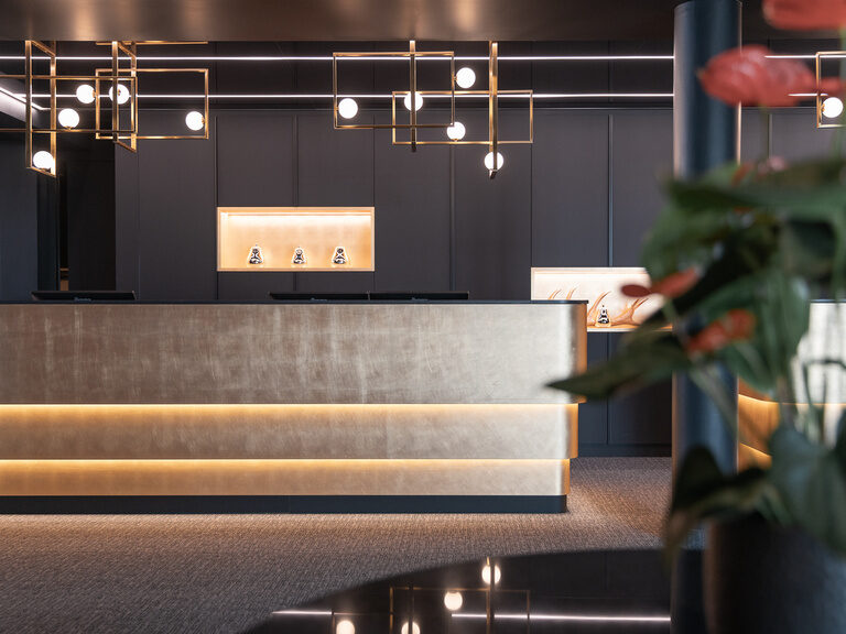 Die Rezeption im Hotel Oswald mit edlem Empfangstresen, stilvoller Beleuchtung und moderner Atmosphäre für einen angenehmen Check-in.