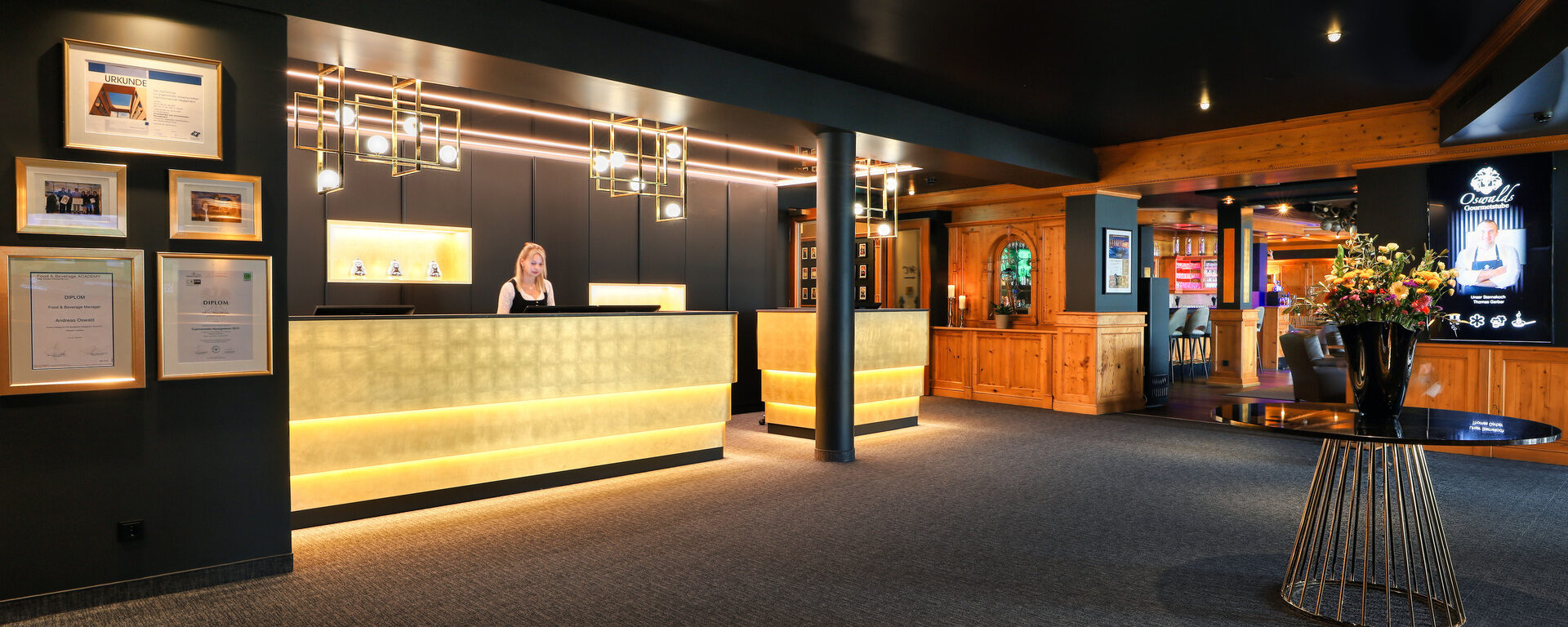 Einladender Empfangsbereich mit beleuchtetem Tresen, modernen Designelementen und herzlichem Service im Hotel Oswald Bayerischer Wald.