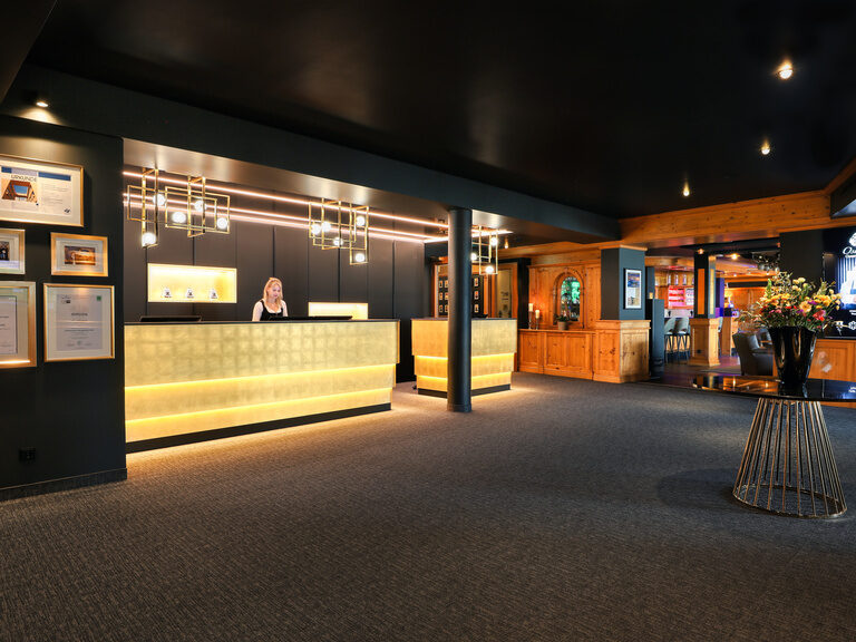 Einladender Empfangsbereich mit beleuchtetem Tresen, modernen Designelementen und herzlichem Service im Hotel Oswald Bayerischer Wald.
