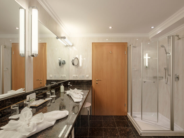 Das elegante Badezimmer der Romantiksuite Plus im Hotel Oswald bietet luxuriösen Komfort mit Doppelwaschbecken, großer Dusche und edlen Marmorflächen.