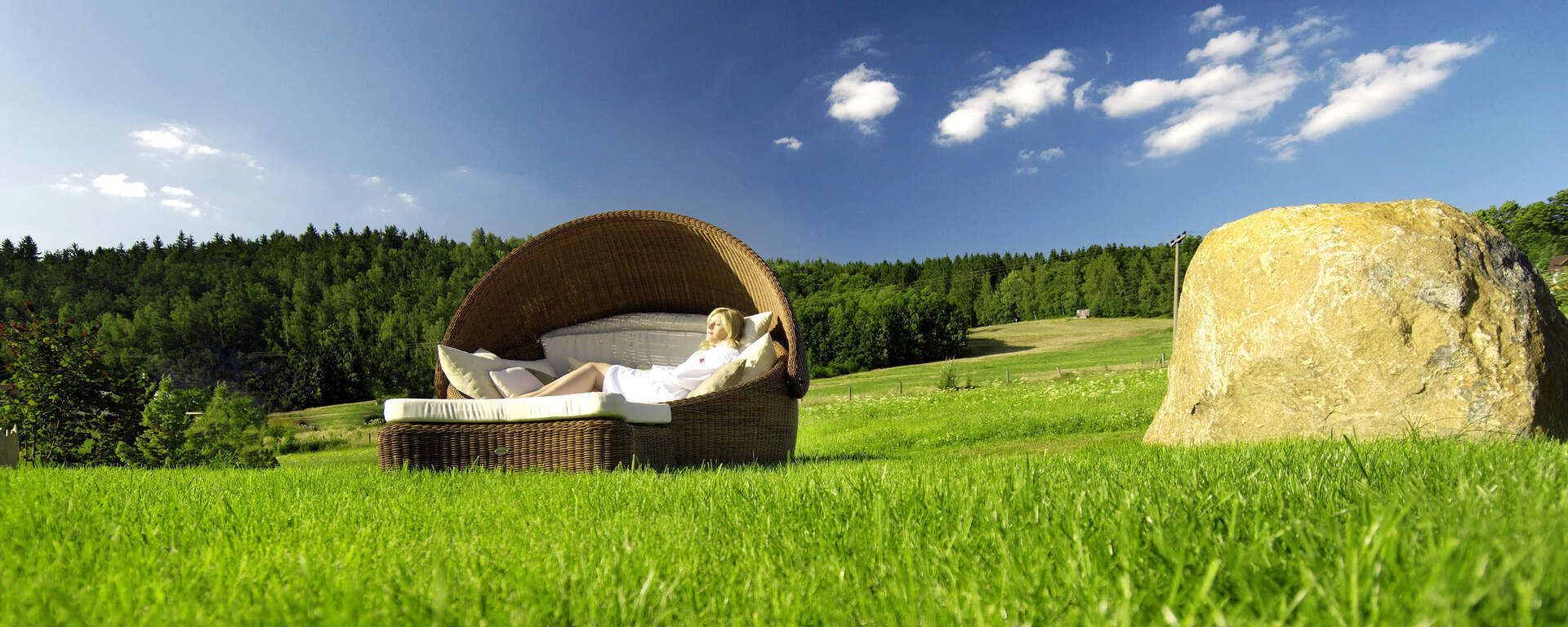 Frau entspannt auf einer Liege im Grünen vor Waldkulisse beim Hotel Oswald im Bayerischen Wald.