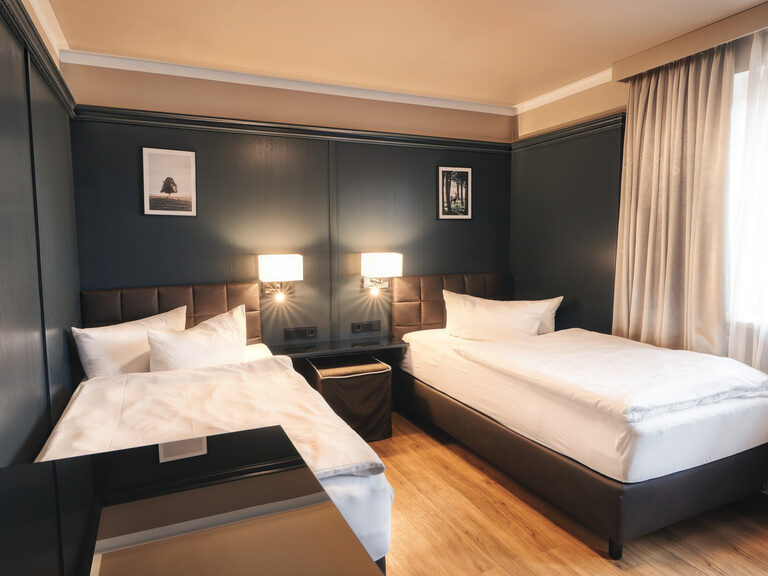 Gut ausgestattetes Hotelzimmer mit zwei Betten und einem modernen Nachttisch im Doppelzimmer Plus 117.
