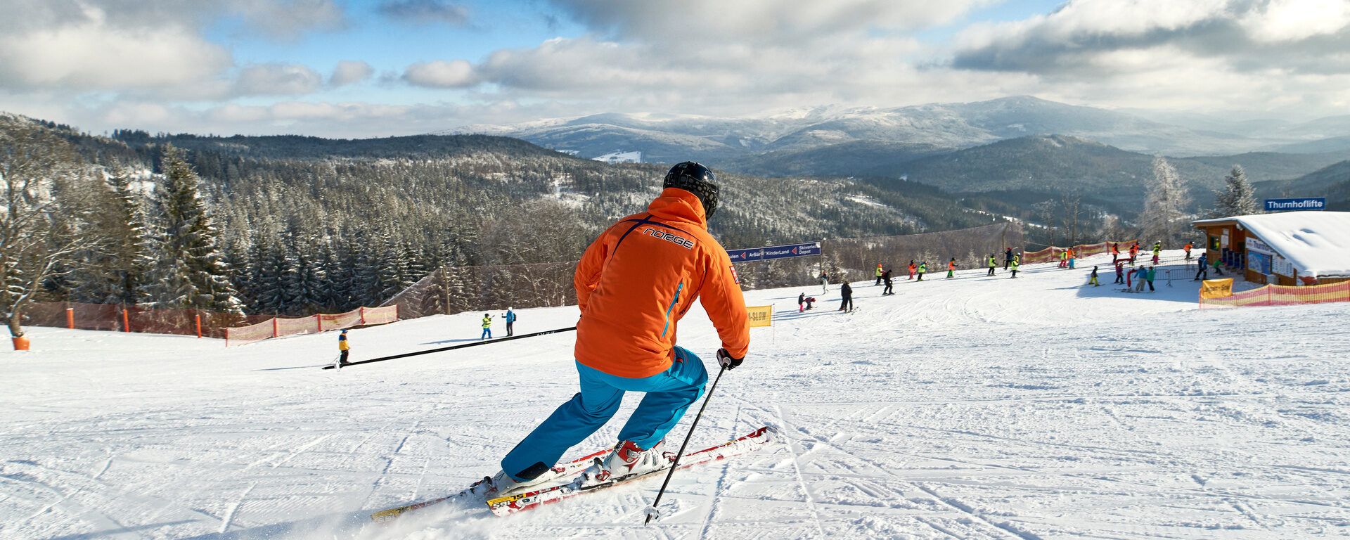 Ein Skifahrer in Bodenmais fährt eine Skipiste runter mit Bayerwald im Hintergrund.