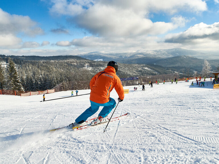 Ein Skifahrer in Bodenmais fährt eine Skipiste runter mit Bayerwald im Hintergrund.