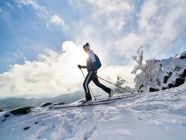 Skitourengeher bei strahlender Sonne nahe einem Gipfelkreuz im verschneiten Bayerischen Wald