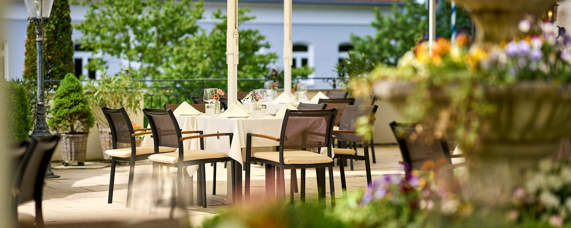 Die gedeckten Tische und Stühle unter Sonnenschirmen im einladenden Gastgarten im Hotel Oswald.