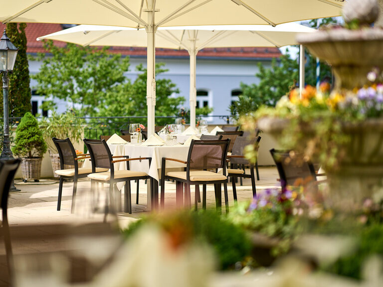 Die gedeckten Tische und Stühle unter Sonnenschirmen im einladenden Gastgarten im Hotel Oswald.