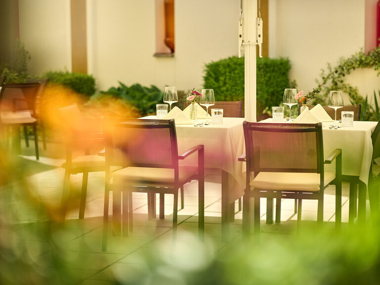 Die Sonnenterrasse im Hotel Oswald mit stilvoll gedeckten Tischen und Blick auf blühende Gartenanlage.