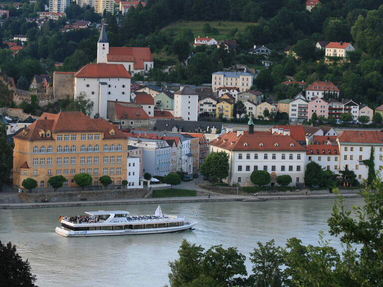 Ausflugsschiff auf der Donau vor der historischen Altstadt von Passau mit Kirche und bunten Häusern.