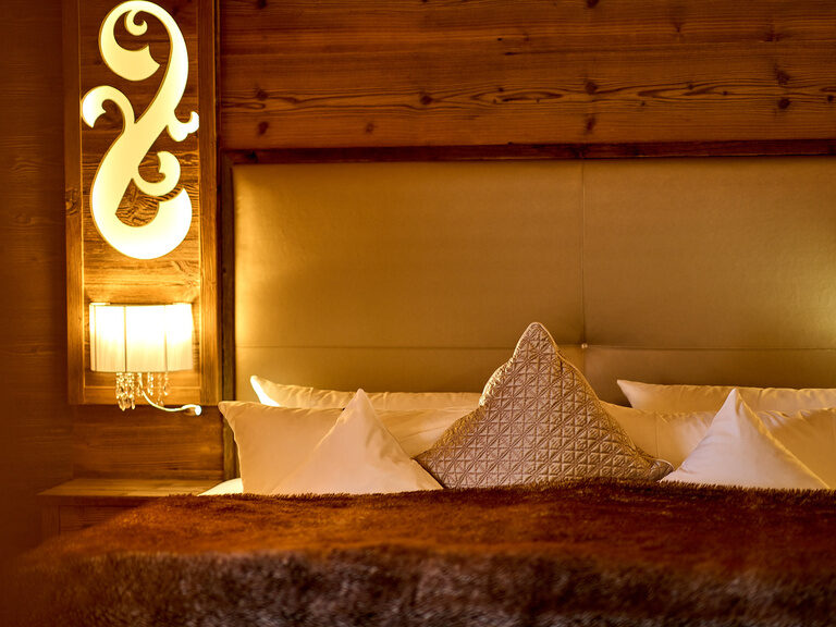 Die Storchennest Plus Suite im Hotel Oswald bietet ein warmes Ambiente mit hochwertigem Holzelementen, einem komfortablen Bett und stimmungsvoller Beleuchtung.