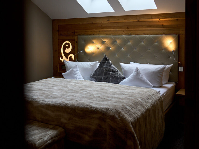 Exklusive Top of Suite "Jagasitz" Plus im Hotel Oswald mit großem Bett, weicher Felldecke und stimmungsvoller Beleuchtung unter Dachfenstern.