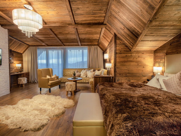 Die Top Suite Storchennest im Hotel Oswald Bayerischer Wald mit edler Holzdecke, gemütlicher Sitzecke und großem Bett im alpinen Stil.