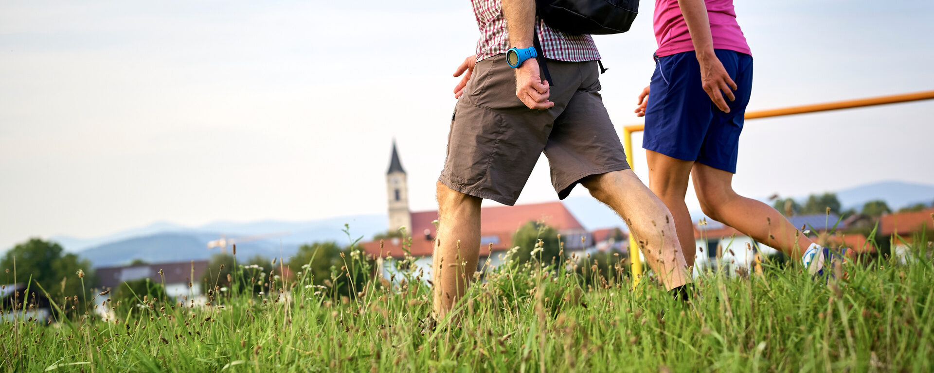 Zwei Personen spazieren mit Rucksäcken durch die weite Graslandschaft im Bayerischen Wald.