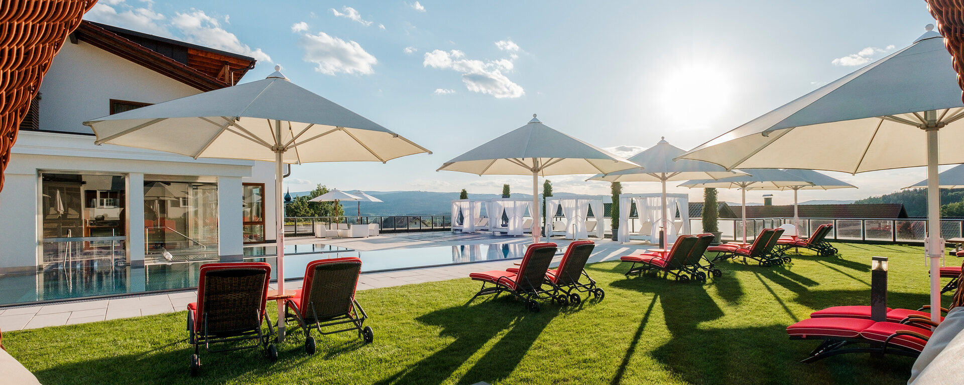 Die Sonne strahlt auf den Wellness-Garten mit Pool und Liegemöglichkeiten vom Hotel Oswald im Bayerischen Wald.